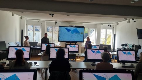 Foto vom Schulungsraum mit PCs und großem Monitor , Referentin Frau Ulbrich, Lableitung Herr Musch und Anwärterin Fr. Hamann begrüßen die Teilnehmerinnen und Teilnehmer